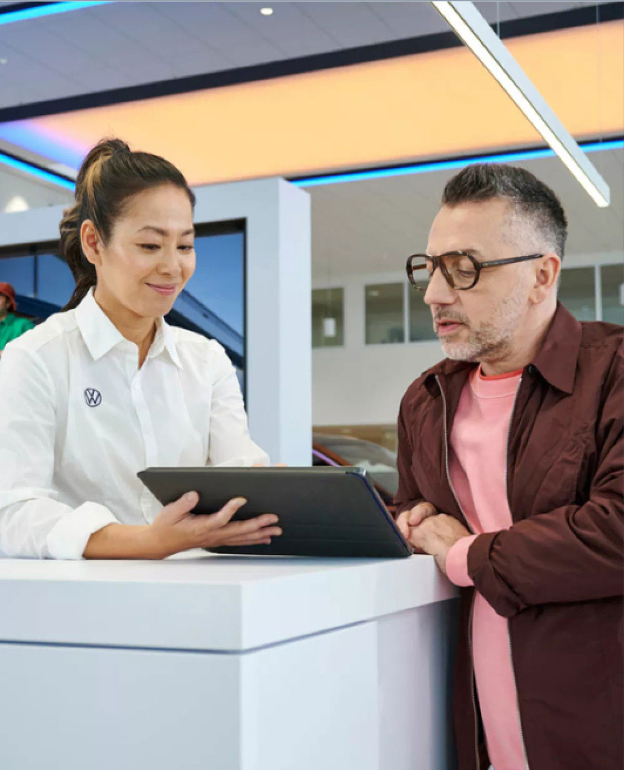 Volkswagen representative assisting a customer with information on a tablet at the dealership counter