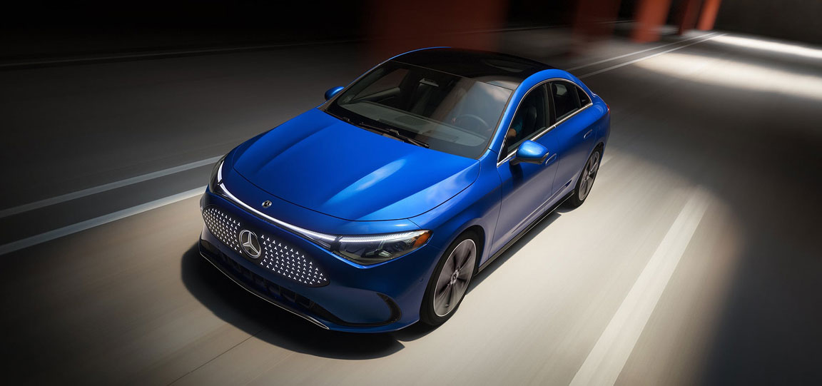blue Mercedes-Benz EQE electric sedan driving through a modern urban setting