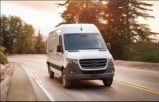 Mercedes-Benz Sprinter cargo van driving on scenic road with trees at sunset