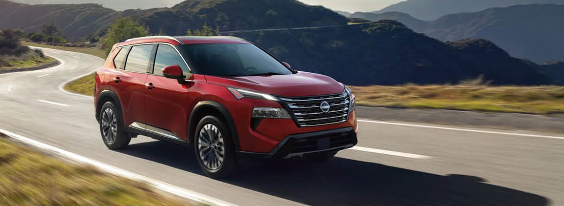 Red Nissan Rogue SUV driving on a scenic mountain highway