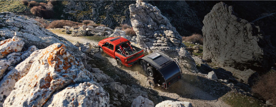 Nissan Frontier towing an off-road camper trailer through rocky trails