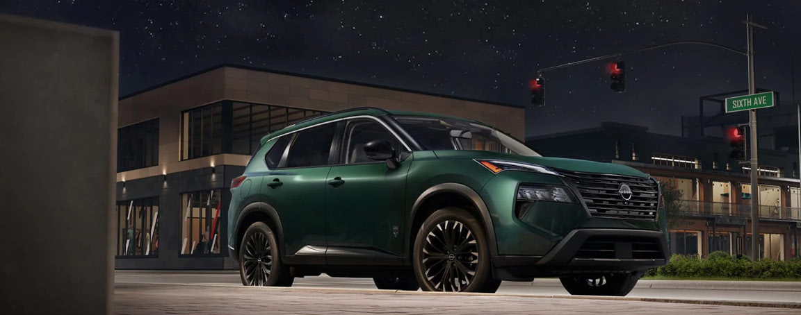 green Nissan Rogue SUV parked on a city street at night with modern buildings in the background