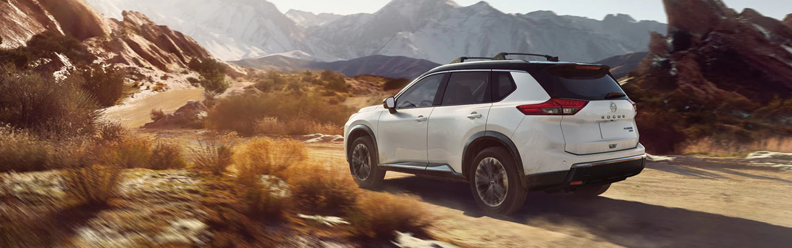 white Nissan Rogue SUV driving through a scenic mountain landscape on a dirt road