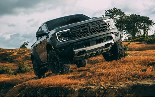 black Ford F-150 Raptor pickup truck climbing rocky terrain during an off-road adventure