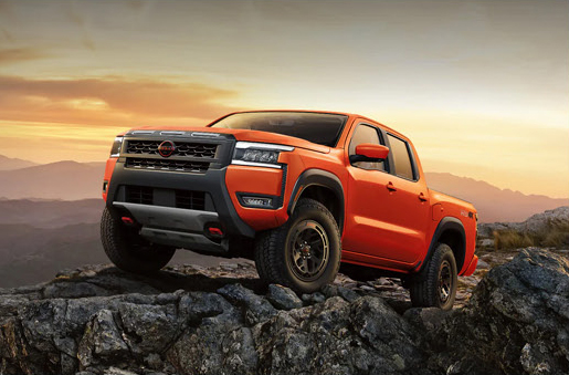 orange Nissan Frontier PRO-4X pickup truck positioned on rocky terrain with mountain views