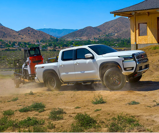 white Nissan Frontier pickup truck towing compact construction equipment near a residential job site