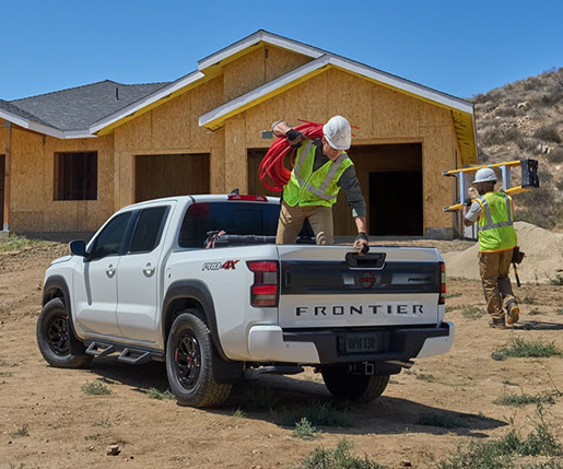 white Nissan Frontier pickup truck parked at a home construction site with workers unloading equipment