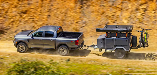 gray Nissan Frontier pickup towing an adventure trailer with outdoor gear on a dirt road
