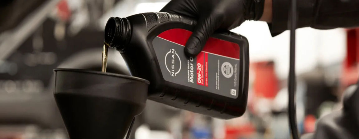Close-up of Nissan Genuine Parts Motor Oil 5W-30 Synthetic Blend being poured into a vehicle engine during a professional oil change service