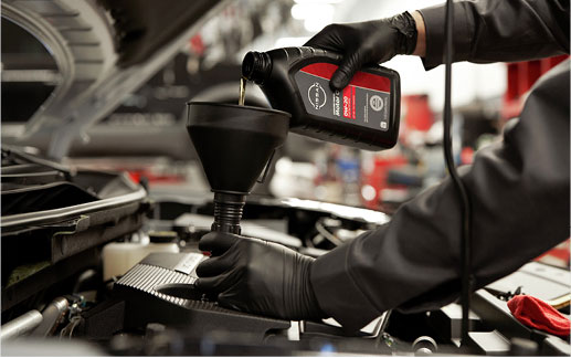 Technician pouring Nissan Genuine Parts Motor Oil 5W-30 Synthetic Blend into a vehicle engine