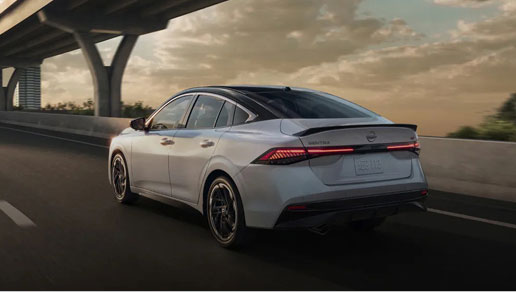 Rear three-quarter view of a silver Nissan Sentra sedan driving on the highway at sunset showcasing LED taillights and aerodynamic styling