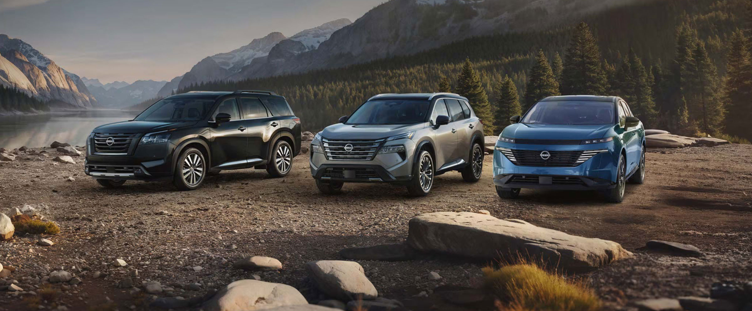 Nissan Pathfinder, Nissan Rogue, and Nissan Ariya SUVs displayed together in a mountain landscape