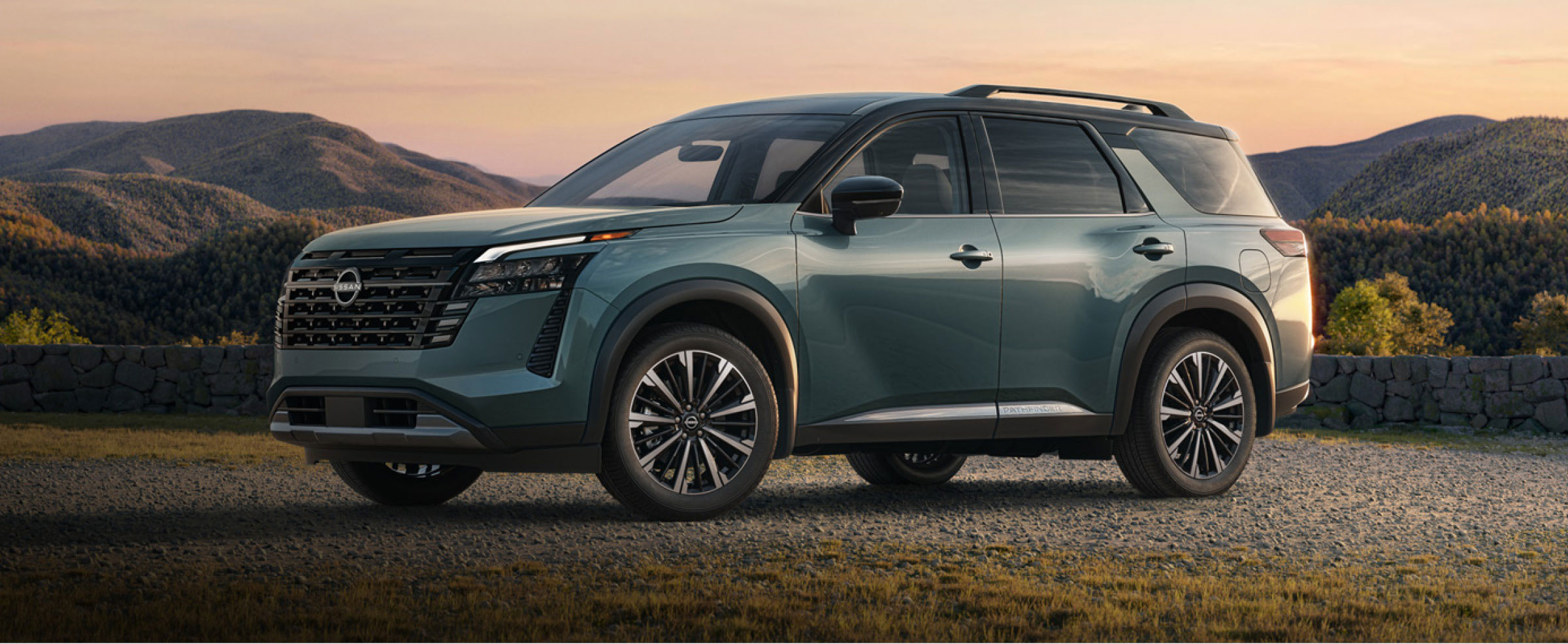 Nissan Pathfinder SUV shown in profile on a scenic mountain road at golden hour
