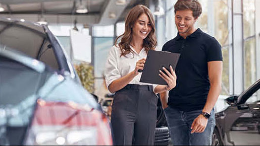 car dealership salesperson showing vehicle details to customer on clipboard