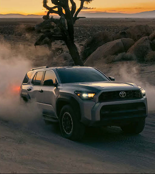 Toyota SUV driving off-road in desert at sunset kicking up dust