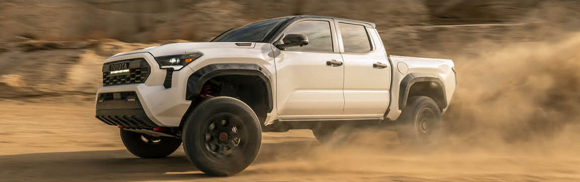 Toyota Tacoma pickup truck in white color driving off road with dust trail