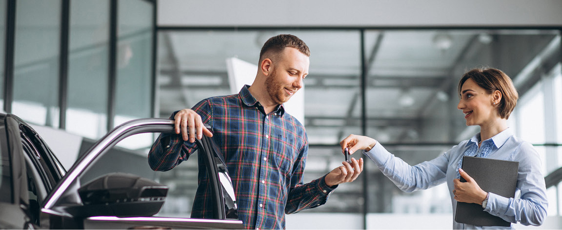 Car dealership sales representative handing keys to happy customer