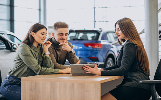 Couple reviewing vehicle purchase details with salesperson at dealership desk