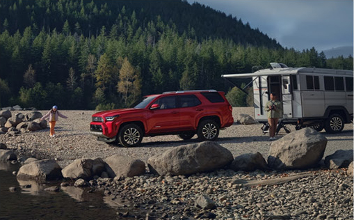 red Toyota 4Runner SUV parked beside a travel trailer at a scenic riverside campsite