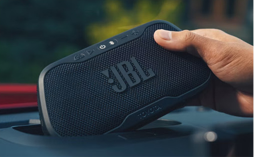 JBL portable Bluetooth speaker held by hand during an outdoor camping or road trip experience