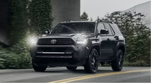 gray Toyota 4Runner SUV driving on a city street with headlights illuminated