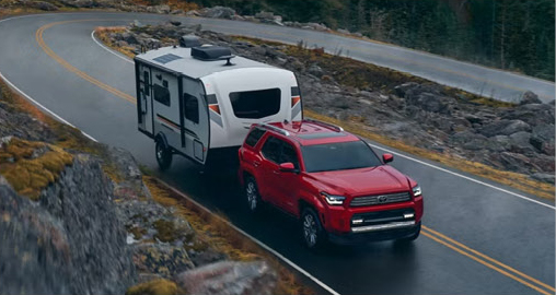 red Toyota 4Runner SUV towing a travel trailer along a winding mountain road