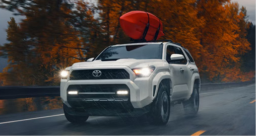 white Toyota 4Runner SUV with a kayak mounted on the roof driving in rainy weather
