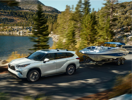 Toyota Grand Highlander towing a boat along a scenic mountain lake road showcasing SUV towing capability