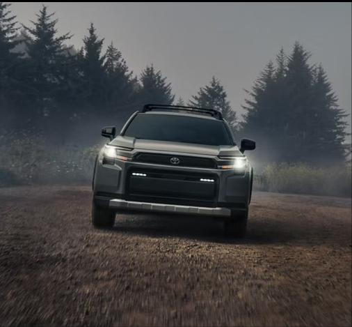front view of a Toyota RAV4 SUV driving on a misty gravel road with headlights illuminated