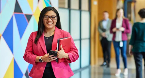business professional holding a smartphone and tablet while standing in a modern office building