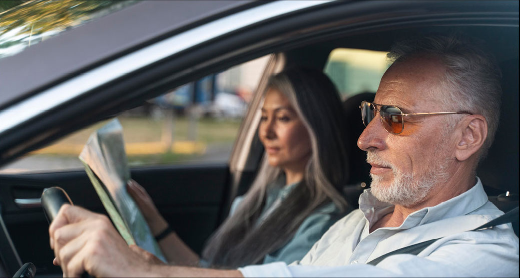 Older man driving while passenger reads map inside vehicle