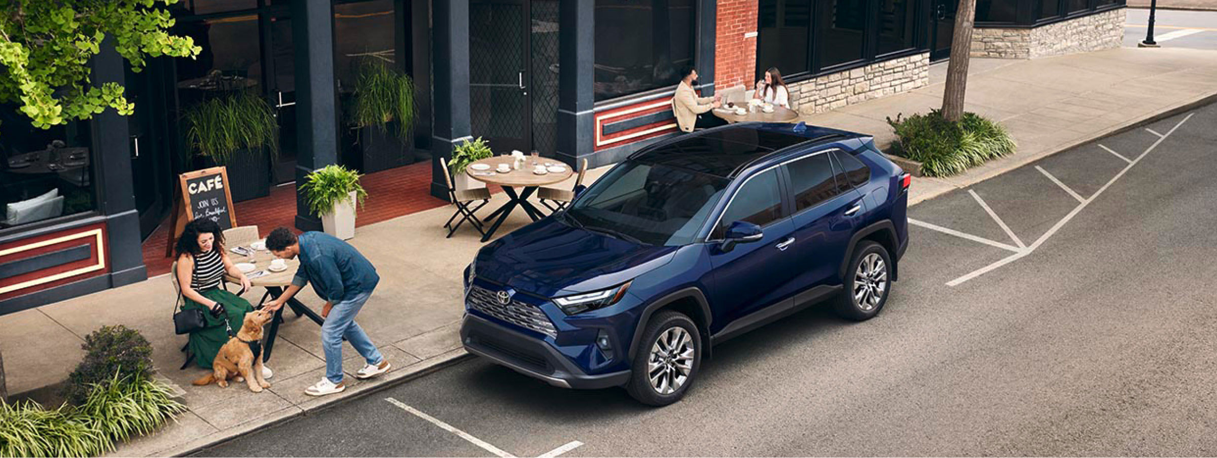 Toyota RAV4 parked on a city street outside a cafe with people sitting outdoors