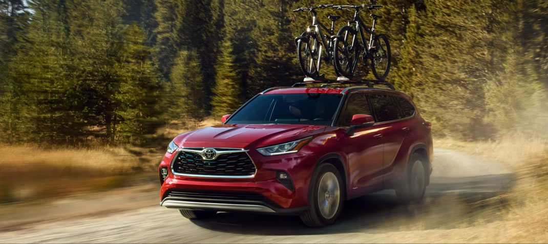 Red Toyota Highlander driving on a dirt road with bicycles mounted on the roof