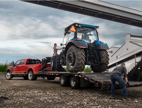 Ford Super Duty truck hauling a tractor on flatbed trailer at worksite