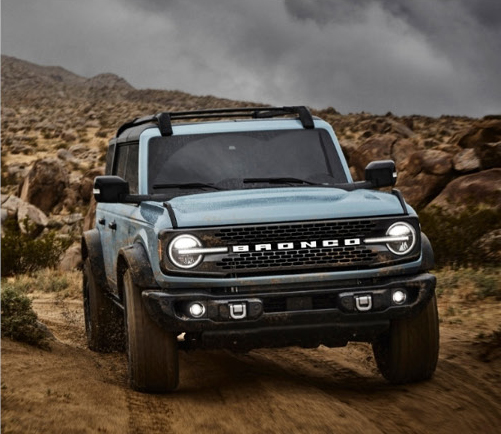 Ford Bronco driving on dirt road in desert landscape