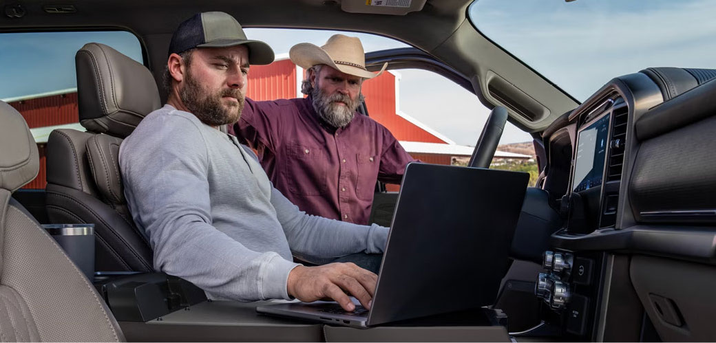 People using a laptop inside a Ford pickup truck interior at a worksite