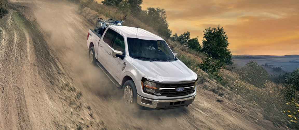 Ford F-150 pickup truck driving off-road on a dirt trail with work equipment in the bed