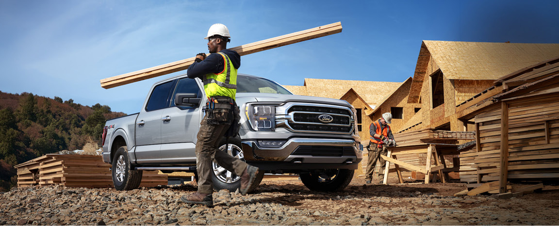 Construction worker carrying lumber near a Ford F-150 pickup truck at a building site