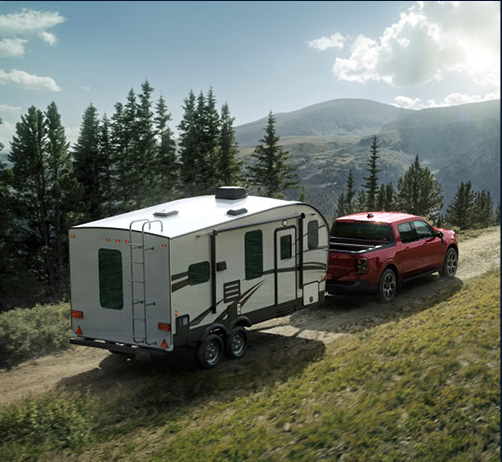 Ford Maverick pickup truck towing a travel trailer along a scenic mountain road
