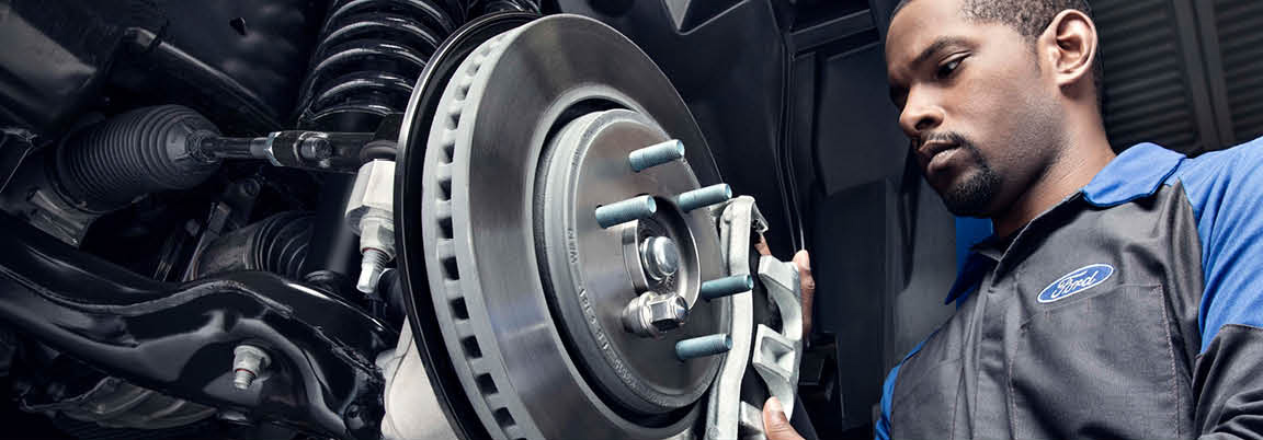 Ford technician inspecting front brake rotor and suspension components during brake service