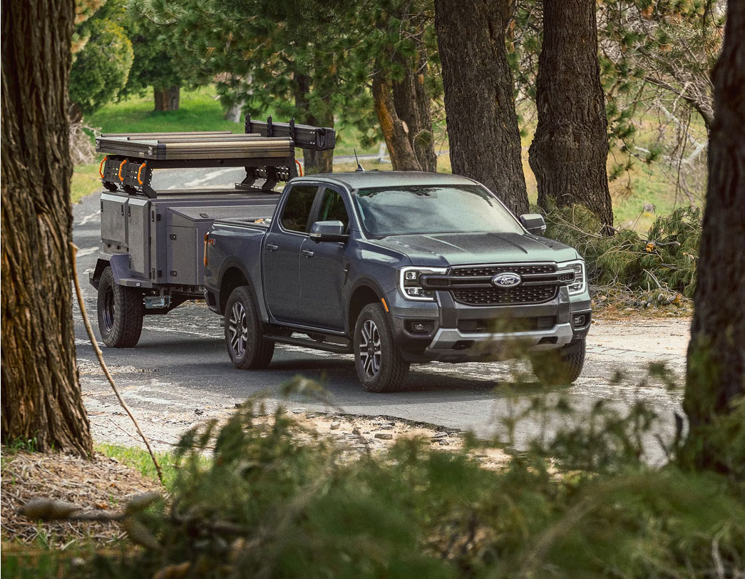Ford Ranger pickup truck towing an off-road camping trailer on a forest road