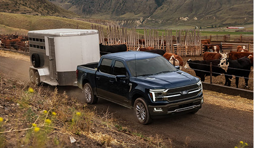 Ford F-150 towing a livestock trailer on a rural farm road