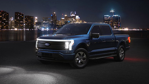 Ford F-150 Lightning electric pickup parked with a city skyline at night