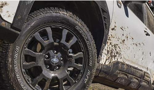 Subaru SUV wheel with Yokohama Geolandar all-terrain tire covered in mud