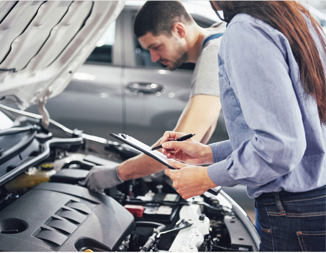 Mechanic inspecting vehicle engine while service advisor takes notes