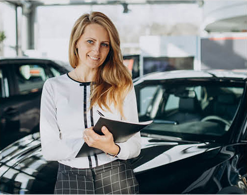 Car dealership sales consultant holding paperwork near vehicles in showroom