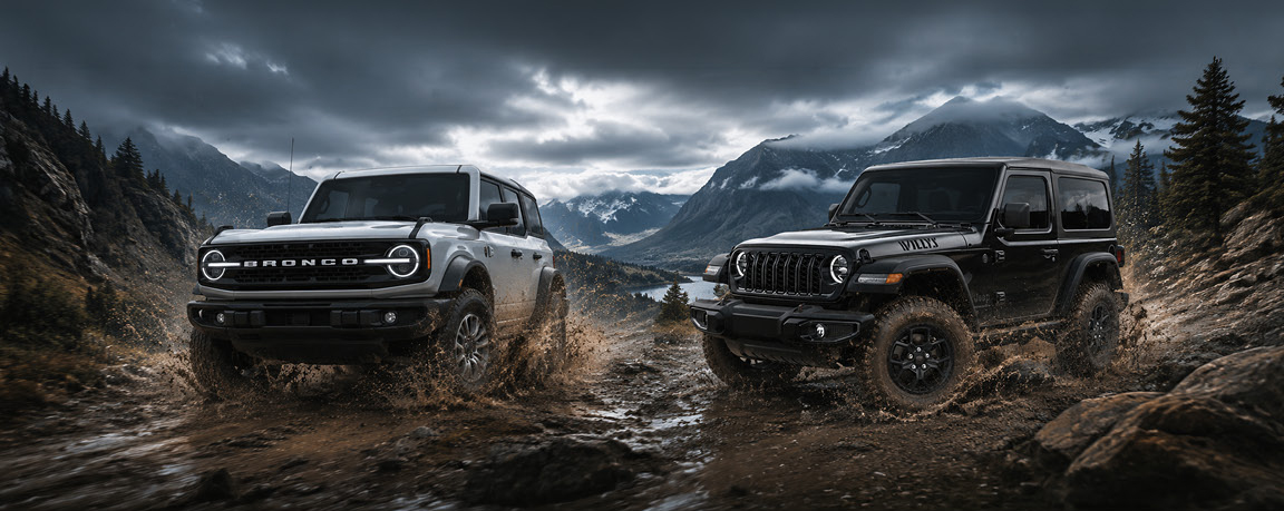 Ford Bronco and Jeep Wrangler driving through muddy mountain terrain during an off-road comparison