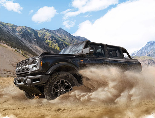 black Ford Bronco SUV driving through desert terrain with dust clouds and mountain scenery