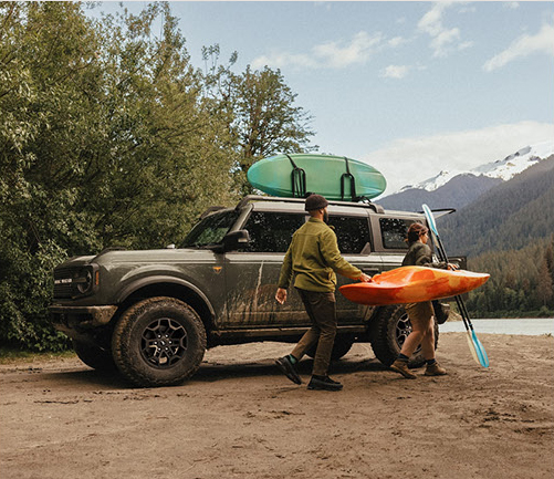Ford Bronco SUV loaded with kayaks parked beside a scenic mountain lake