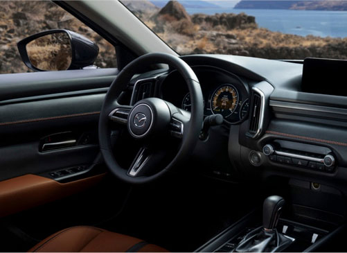 Mazda CX-70 interior cockpit showcasing premium materials, driver-focused controls, and refined cabin design with scenic coastal views